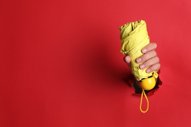 Photo of Woman holding yellow umbrella through hole in red paper, closeup. Space for text