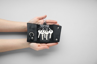 Woman holding open leather holder with keys on light grey background, top view