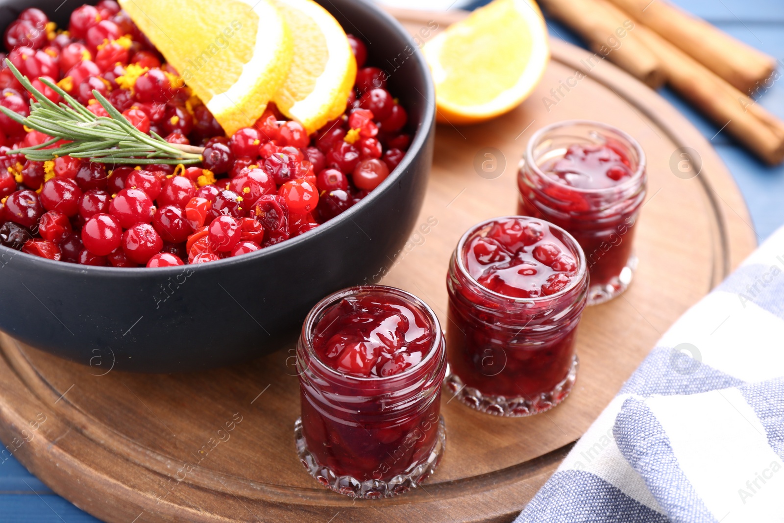 Photo of Cranberries in bowl, jars with sauce and ingredients on blue wooden table, closeup