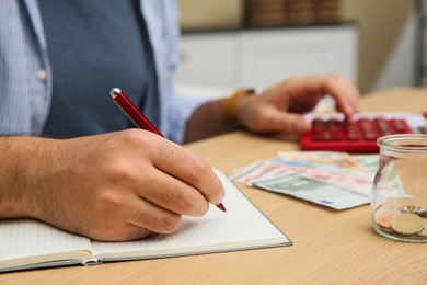 Man counting money with calculator at table indoors, closeup