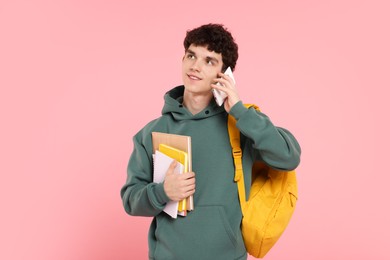 Photo of Portrait of student with backpack and notebooks talking on phone against pink background