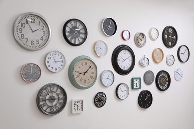 Photo of Collection of different clocks hanging on white wall