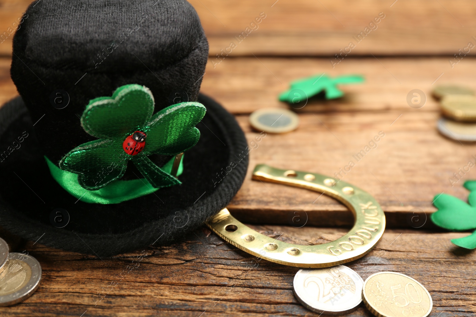 Photo of Leprechaun hat, decorative clover leaves, horseshoe and coins on wooden table, closeup view with space for text. St Patrick's Day celebration