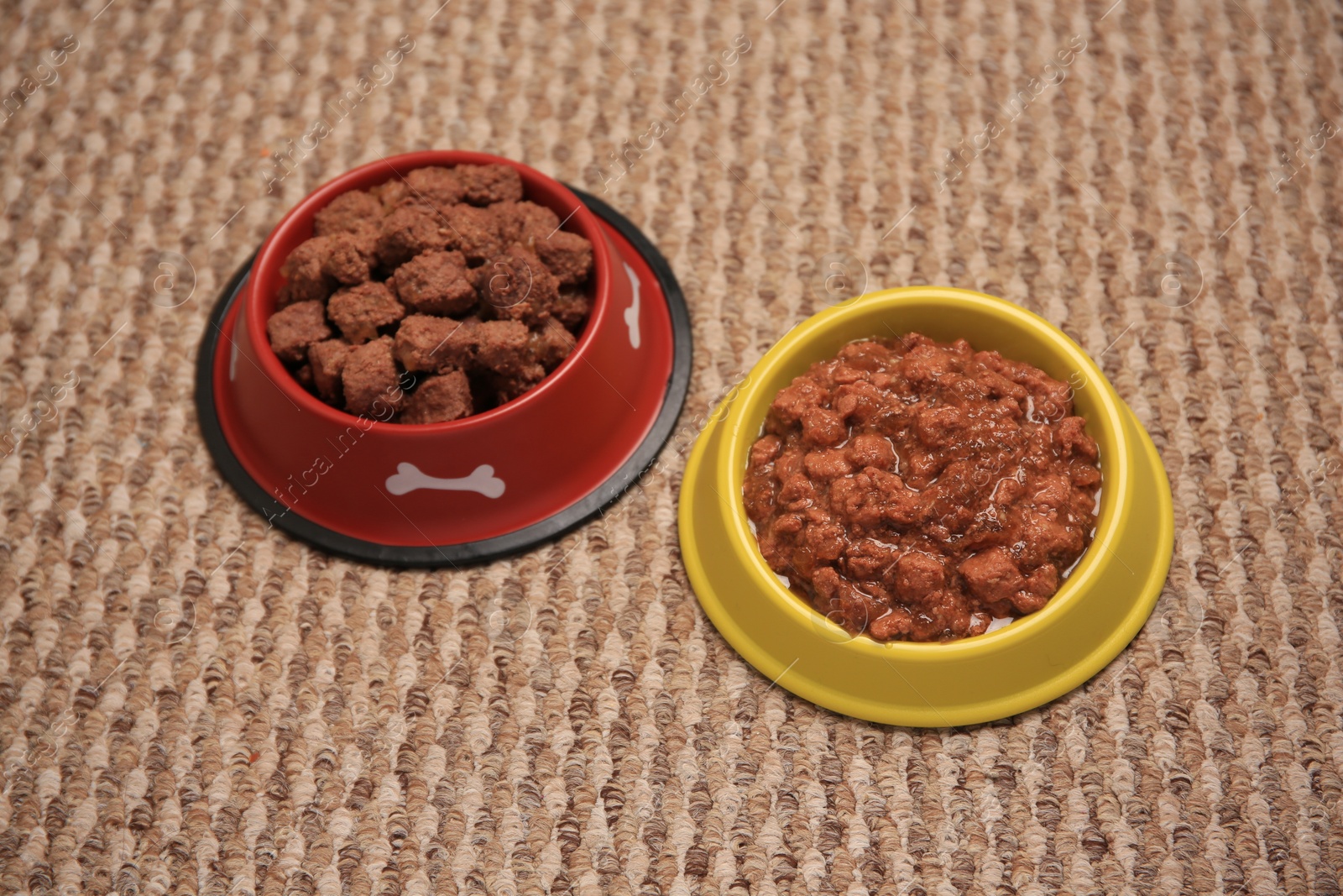 Photo of Wet pet food in feeding bowls on soft carpet, above view