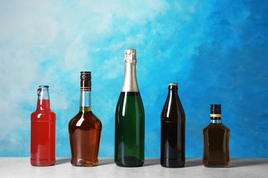 Bottles with different alcoholic drinks on table against color background