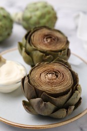 Photo of Delicious cooked artichokes with tasty sauce on table, closeup