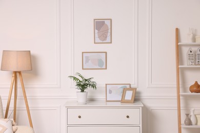 Photo of Picture frames hanging on white wall and chest of drawers at home