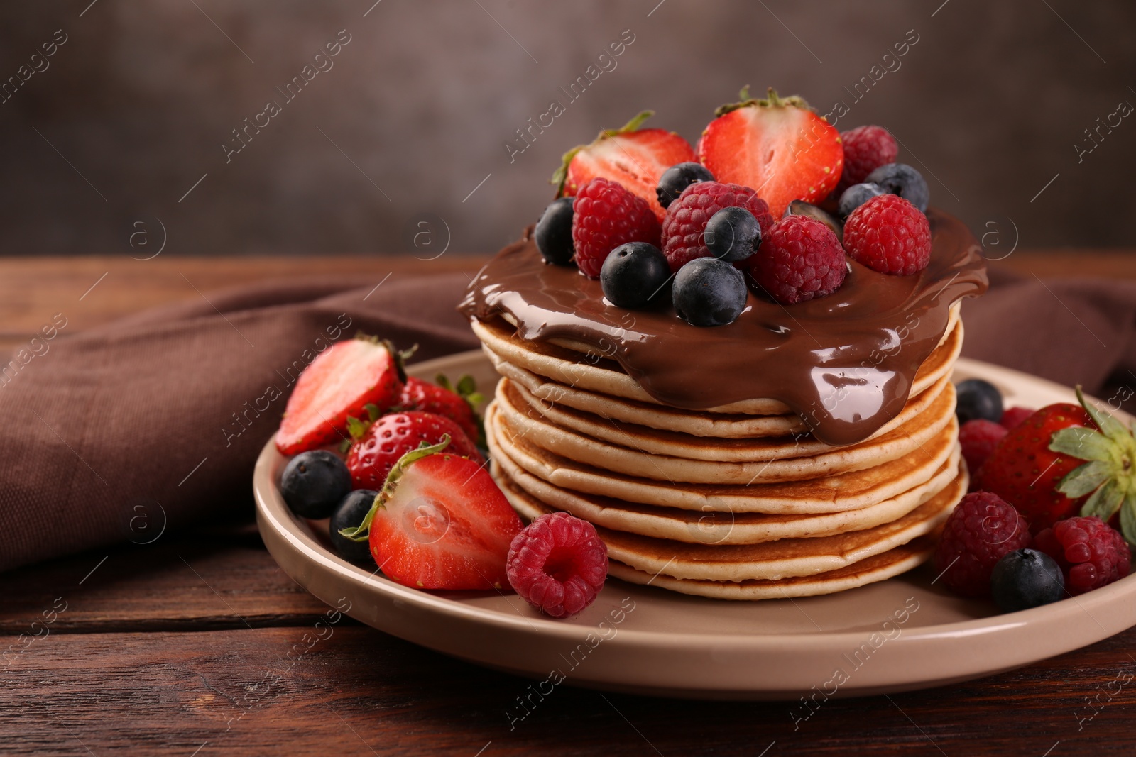 Photo of Stack of tasty pancakes with fresh berries and chocolate spread on wooden table, closeup