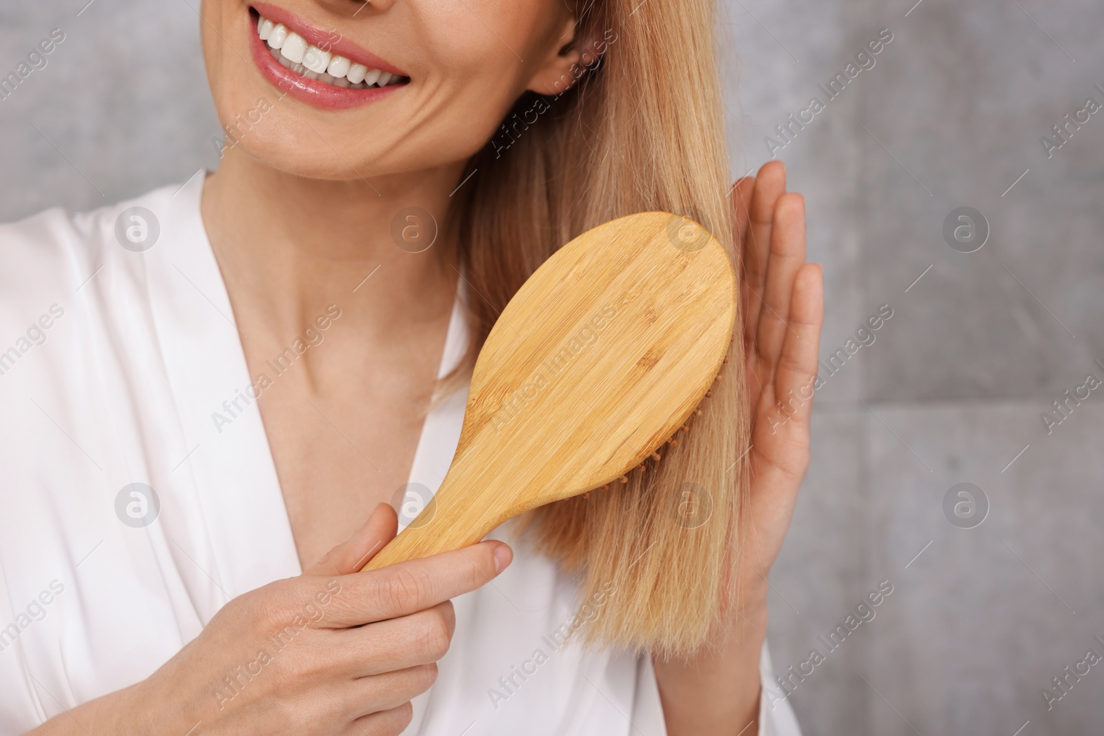 Photo of Woman in white robe brushing her hair indoors, closeup