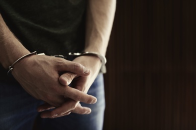 Man detained in handcuffs against blurred wooden background, space for text. Criminal law