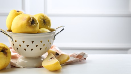 Photo of Tasty ripe quinces and metal colander on white wooden table, closeup. Space for text
