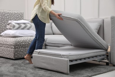 Woman making sleeping place for guest in living room, closeup. Convertible sofa