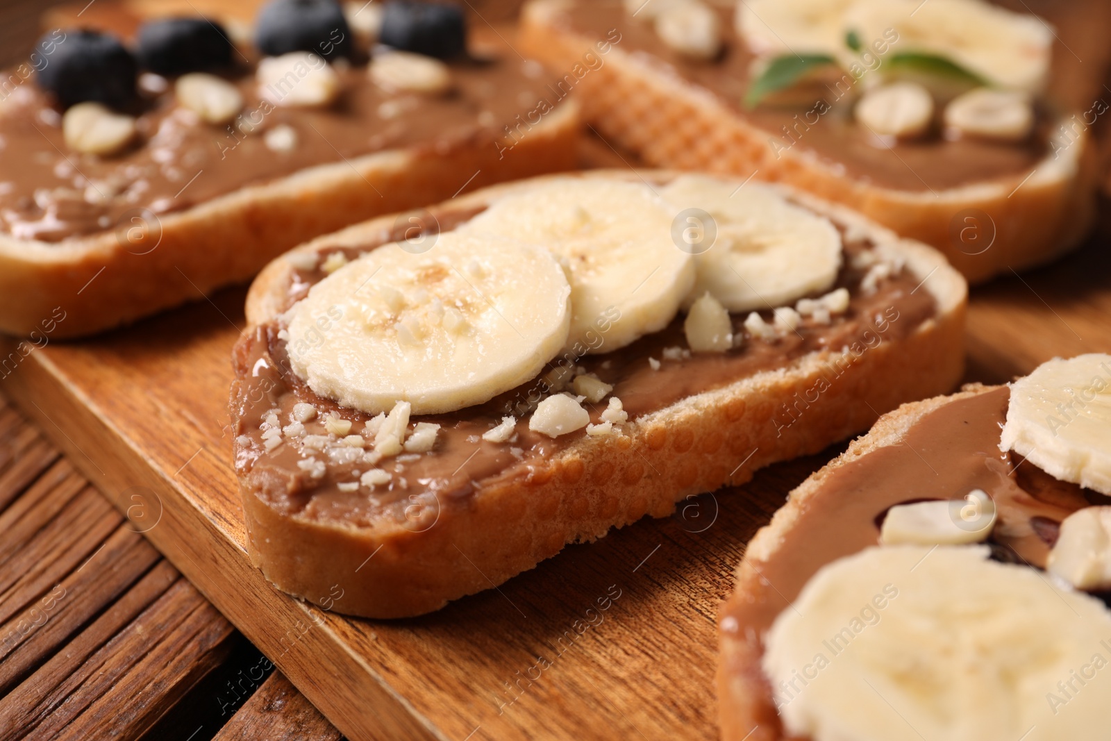 Photo of Toasts with tasty peanut butter, banana slices and nuts on wooden table, closeup