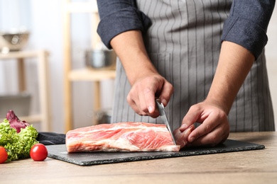 Photo of Man cutting fresh raw meat on wooden table in kitchen, closeup