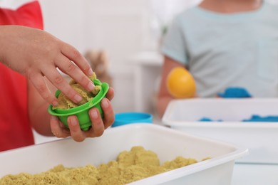 Photo of Little children playing with bright kinetic sand at table indoors, closeup