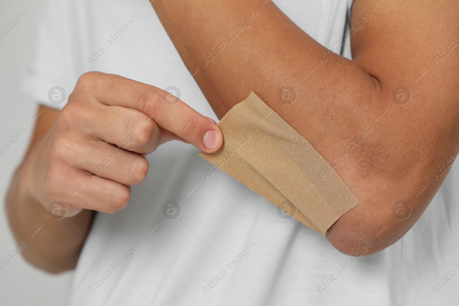 Photo of Man putting sticking plaster onto elbow, closeup
