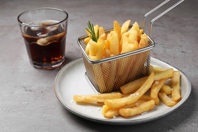 Photo of Tasty french fries with rosemary and soda drink on light grey table
