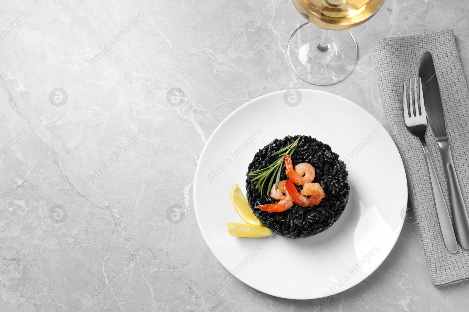 Photo of Delicious black risotto with shrimps served on grey marble table, flat lay. Space for text