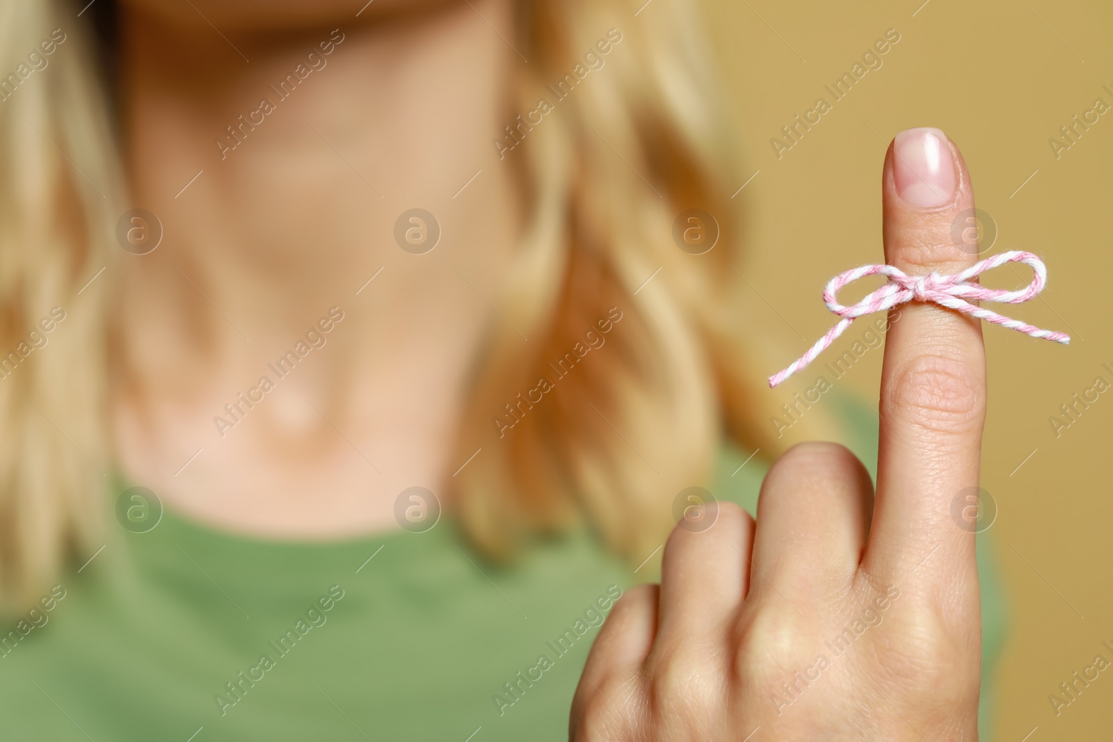 Photo of Woman showing index finger with tied bow as reminder against light brown background, focus on hand