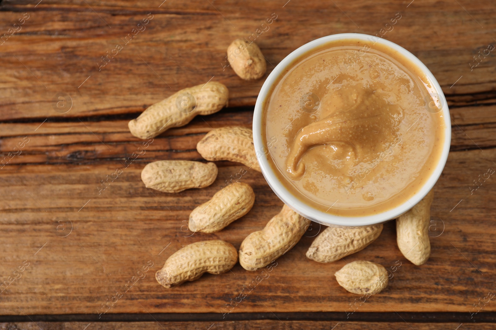 Photo of Delicious nut butter in bowl and peanuts on wooden table, top view