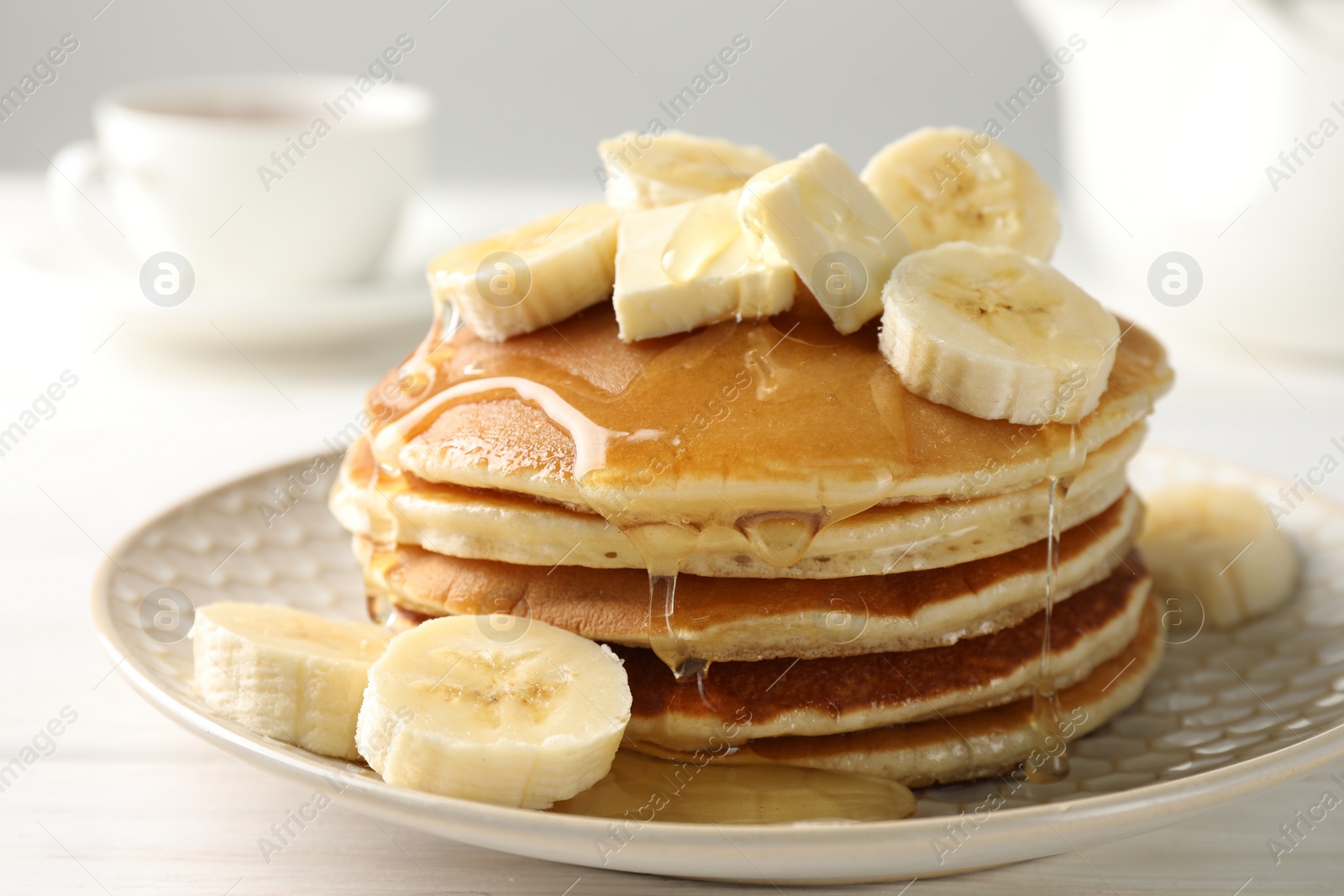 Photo of Delicious pancakes with bananas, honey and butter on white wooden table, closeup