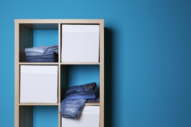 Photo of Stack of different jeans in wardrobe against color wall with space for text