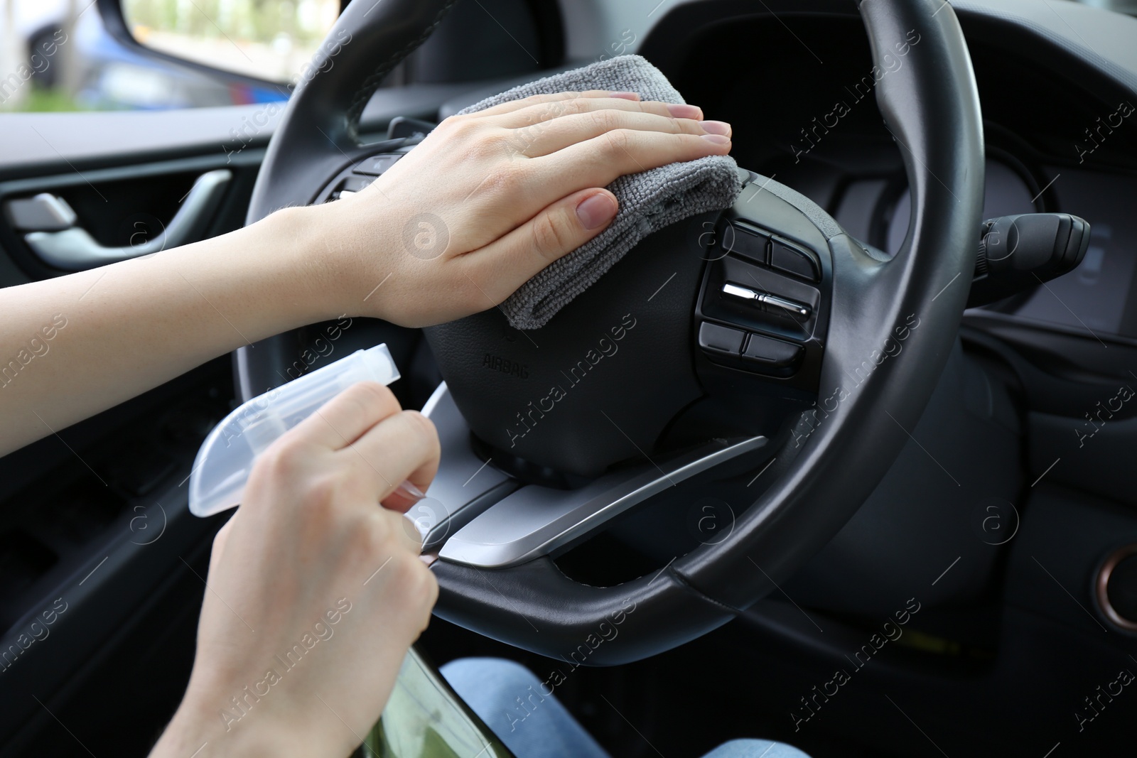 Photo of Woman cleaning steering wheel with rag in car, closeup