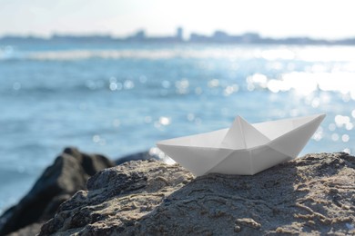 Photo of White paper boat on rock near sea, space for text