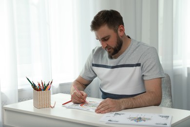 Young man coloring antistress picture at table indoors