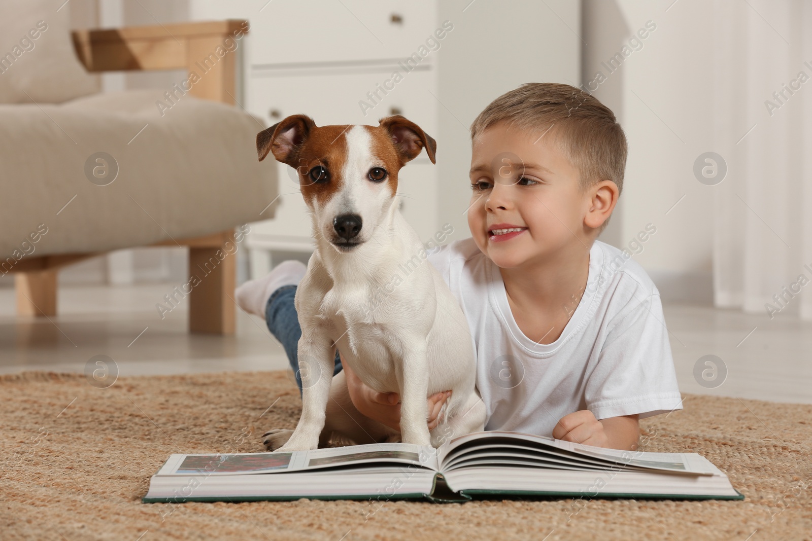 Photo of Little boy with book and his cute dog on floor at home. Adorable pet