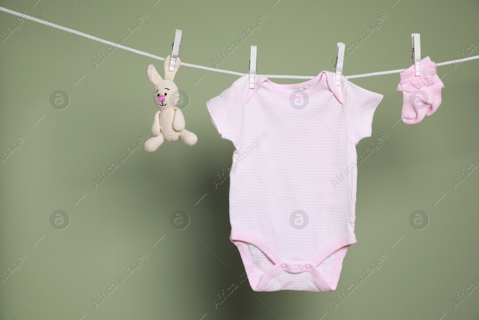 Photo of Cute small baby clothes and toy hanging on washing line against green background