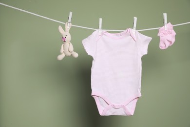 Photo of Cute small baby clothes and toy hanging on washing line against green background