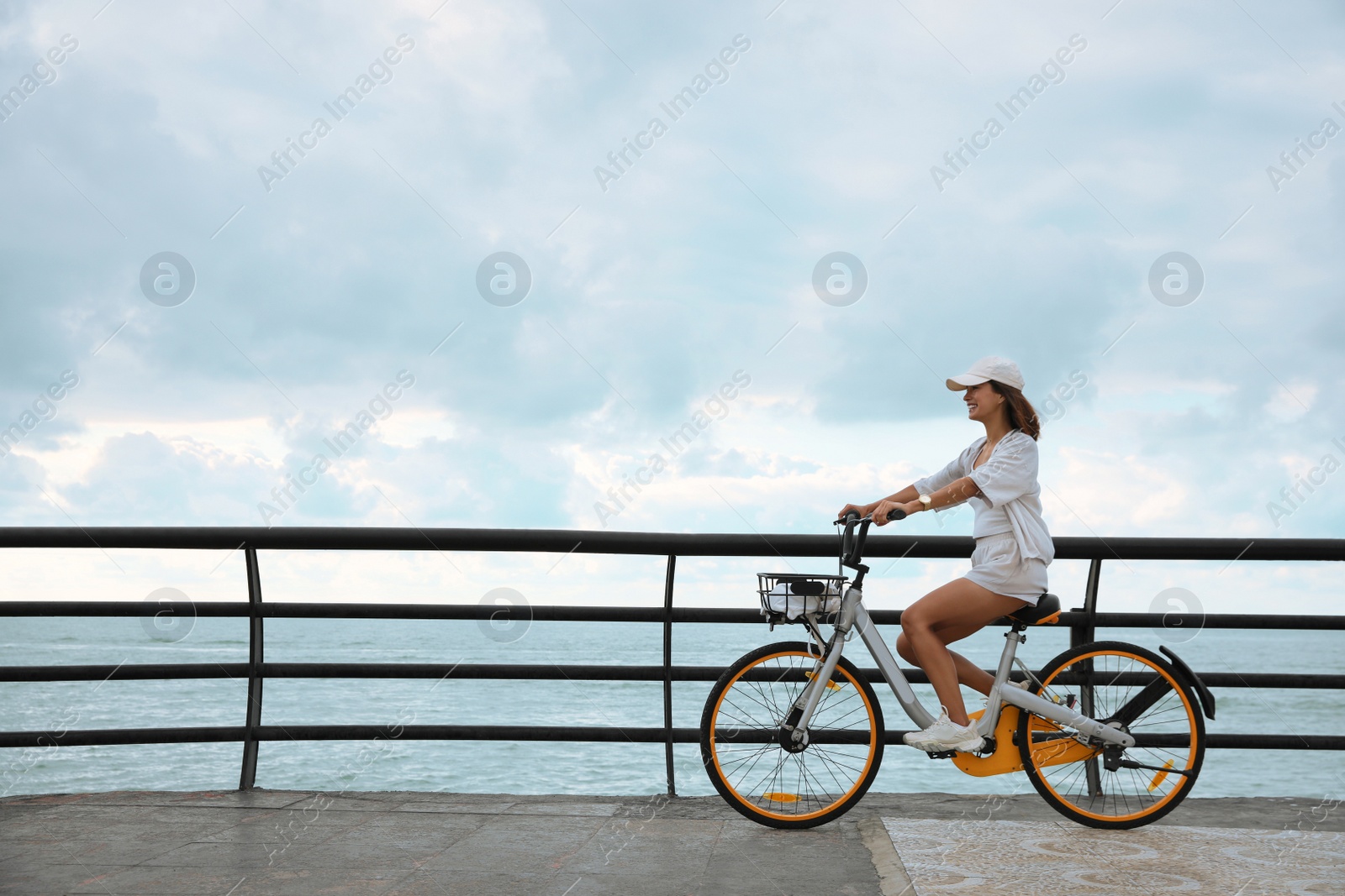 Photo of Beautiful young woman riding bicycle along embankment. Space for text