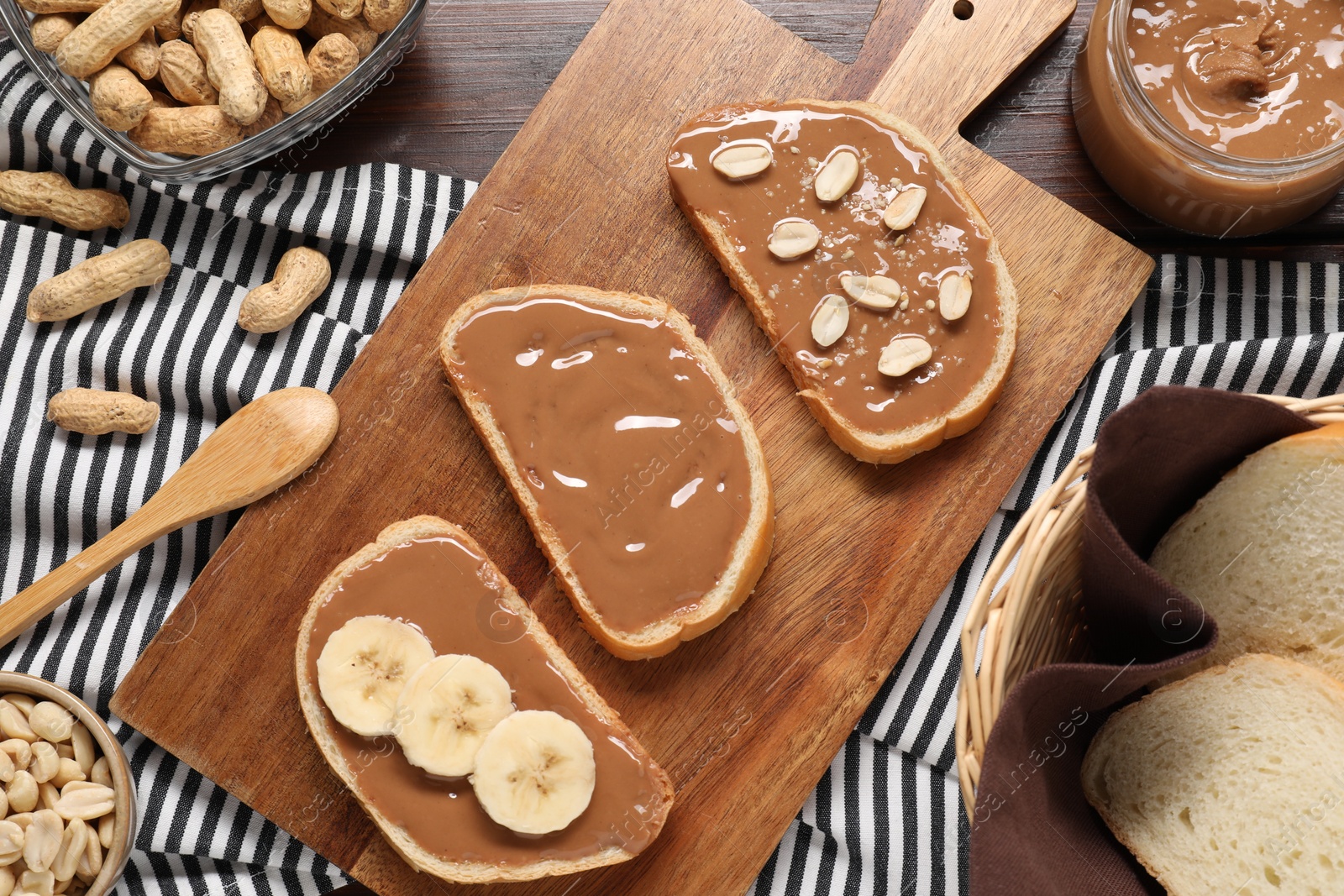 Photo of Toasts with tasty nut butter, banana slices and peanuts on wooden table, flat lay