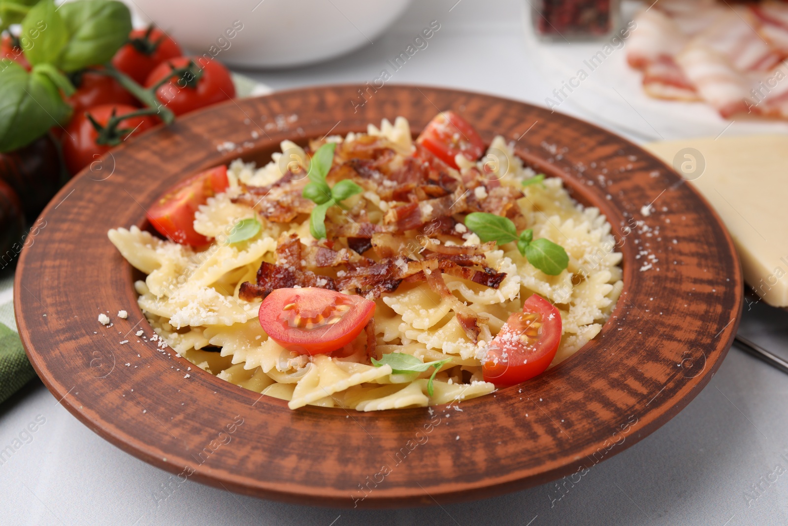 Photo of Tasty pasta with bacon, tomatoes and basil on white tiled table