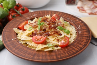 Tasty pasta with bacon, tomatoes and basil on white tiled table