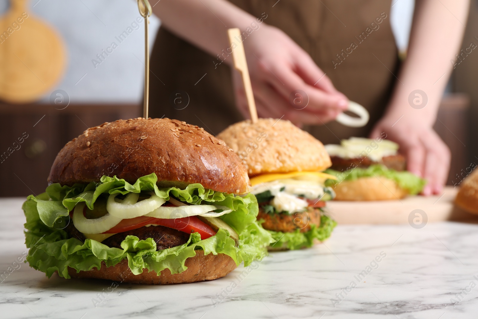 Photo of Woman making delicious vegetarian burger at white marble table, selective focus