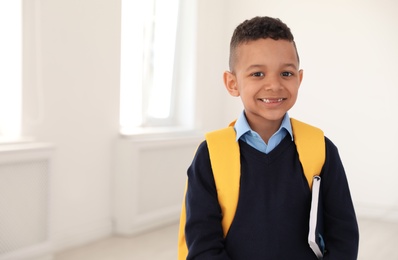Photo of Portrait of cute African-American boy in school uniform with backpack and book indoors. Space for text