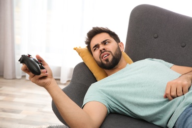 Photo of Lazy young man playing video game while lying on sofa at home