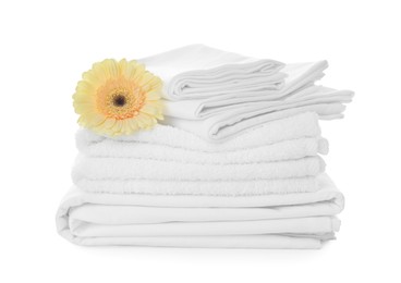 Photo of Stack of towels and bed sheets with gerbera on white background
