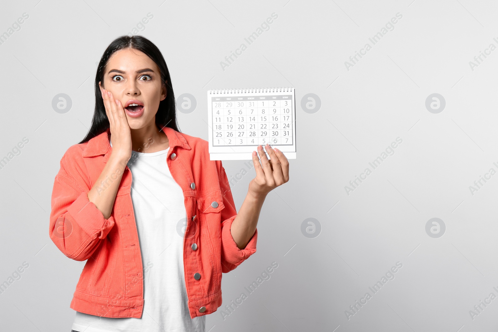 Photo of Emotional young woman holding calendar with marked menstrual cycle days on light background. Space for text