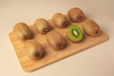 Wooden board with whole kiwis and cut one on beige background