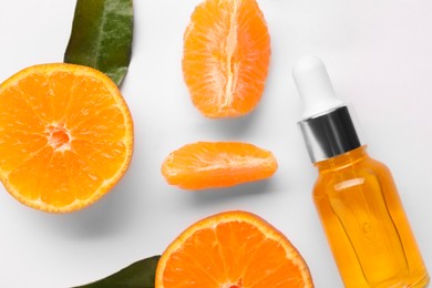 Aromatic tangerine essential oil in bottle, leaves and citrus fruits on white table, flat lay