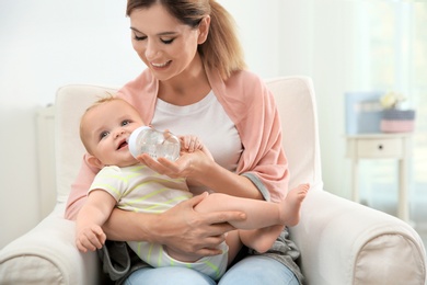 Photo of Lovely mother giving her baby drink from bottle in room
