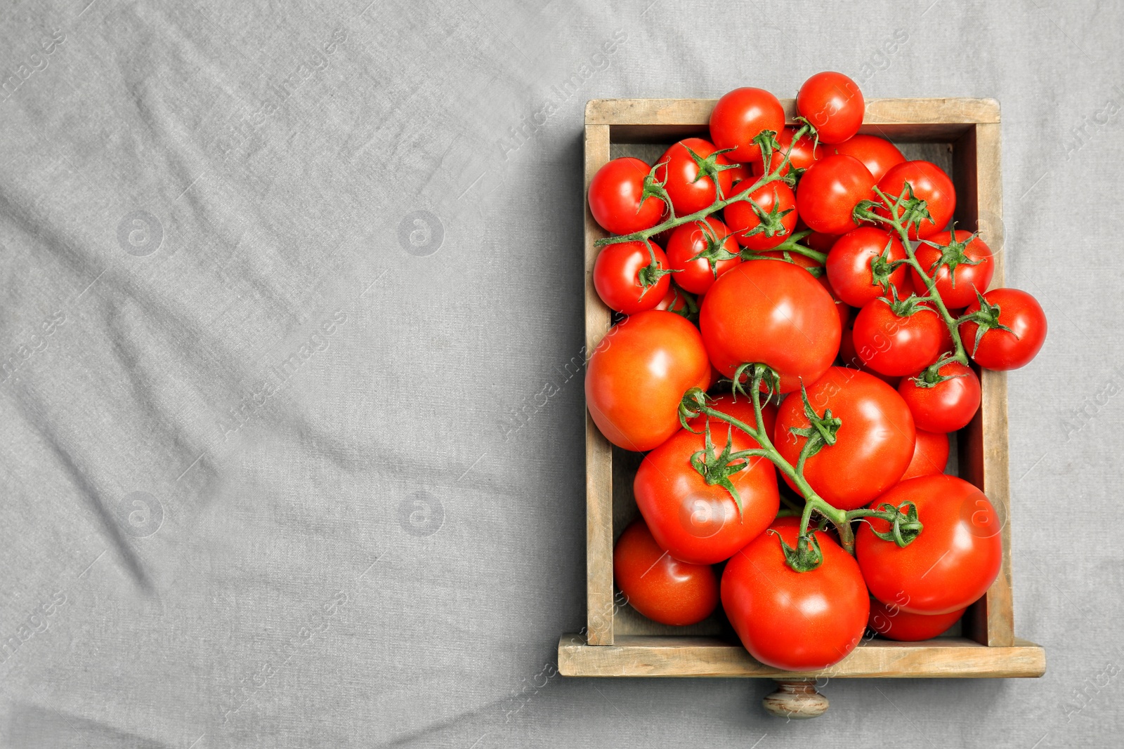 Photo of Wooden crate with fresh ripe tomatoes on grey fabric