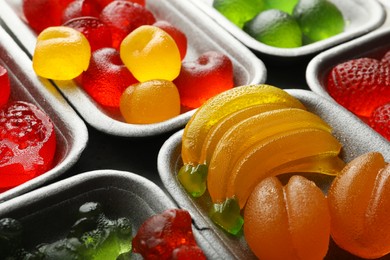 Photo of Different delicious gummy candies in containers, closeup