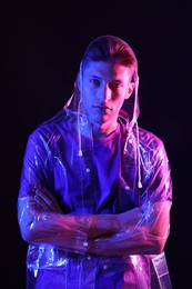 Young man wearing clear coat on dark background in neon lights