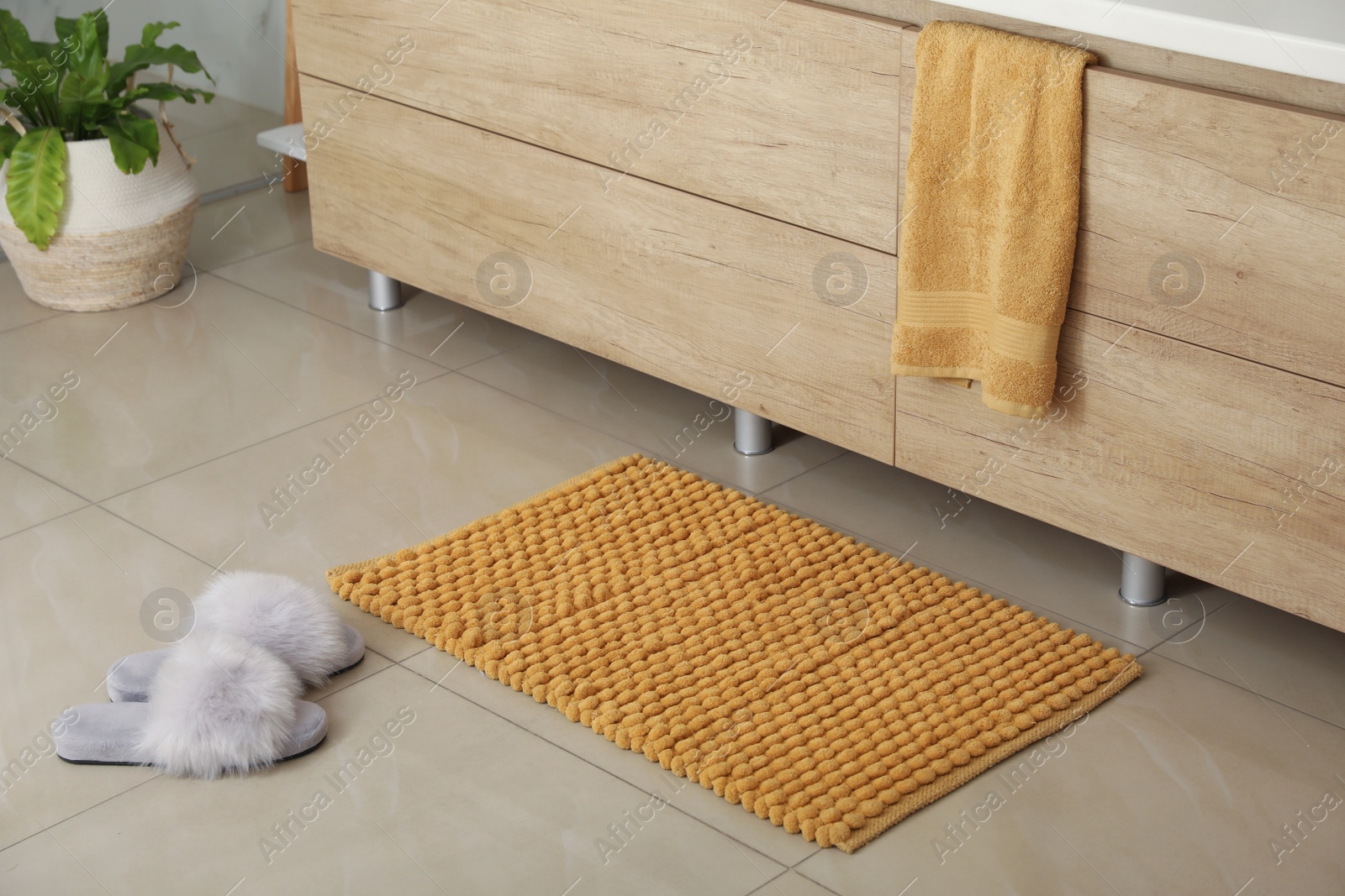 Photo of Soft orange bath mat and slippers on floor indoors