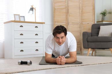 Overweight man doing plank exercise on mat at home