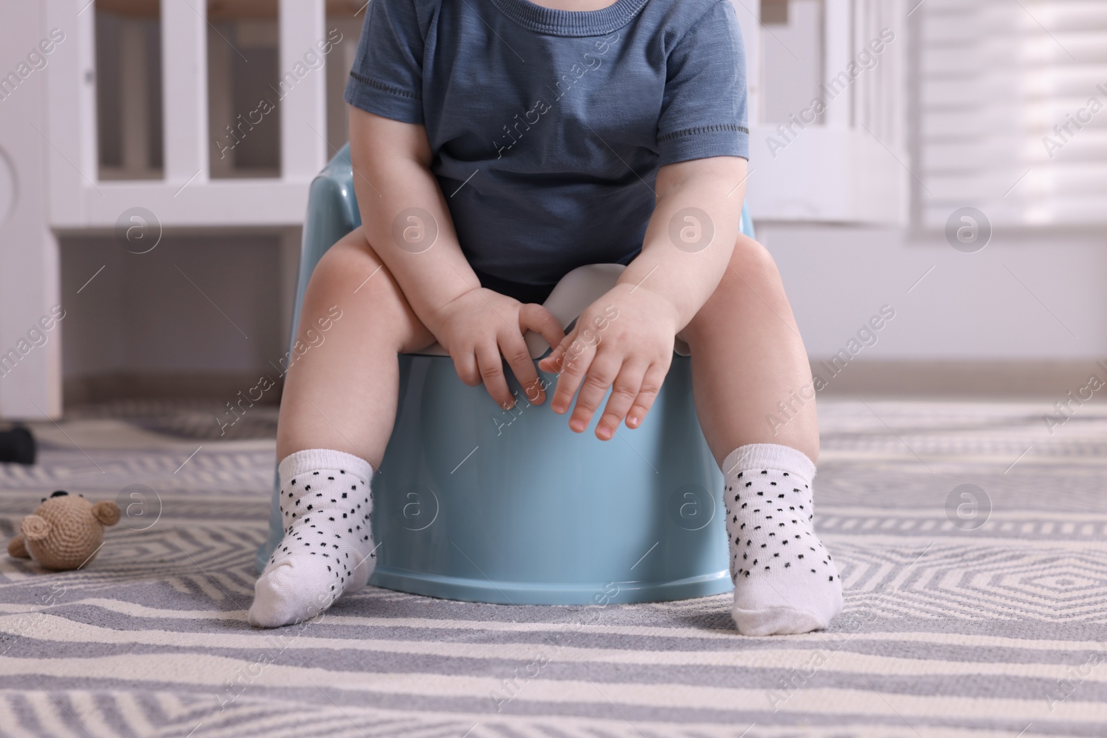 Photo of Little child sitting on plastic baby potty indoors, closeup